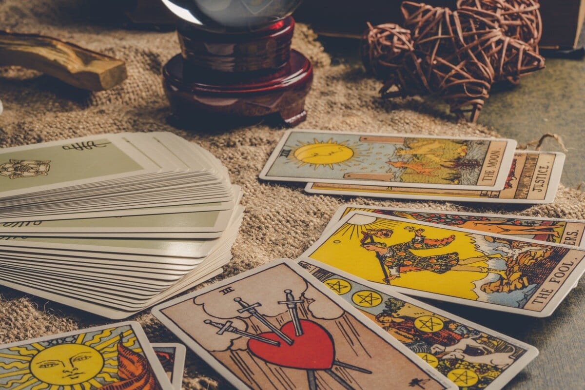 Hands holding The Sun tarot card above a spread of cards on burlap cloth
